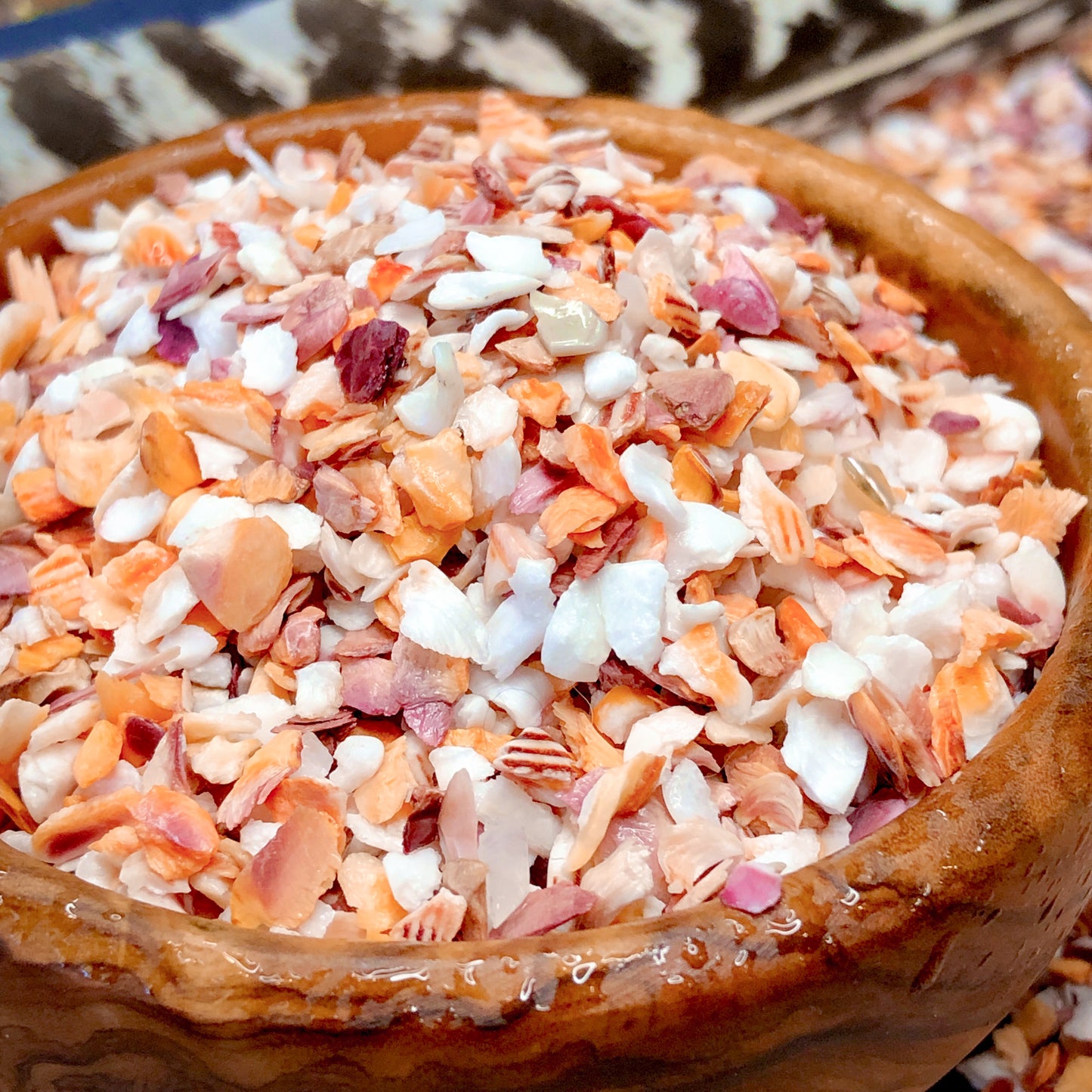 A wooden bowl filled with orange, purple, and white crushed mano de lion shells. Also, known as "paw of the lion", these tiny shells are 2-4 millimeters and great for your beach themed art project.