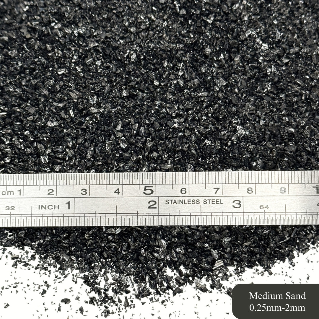 Black tourmaline sand with a ruler showing particle size, labeled '0.25mm-2mm'.