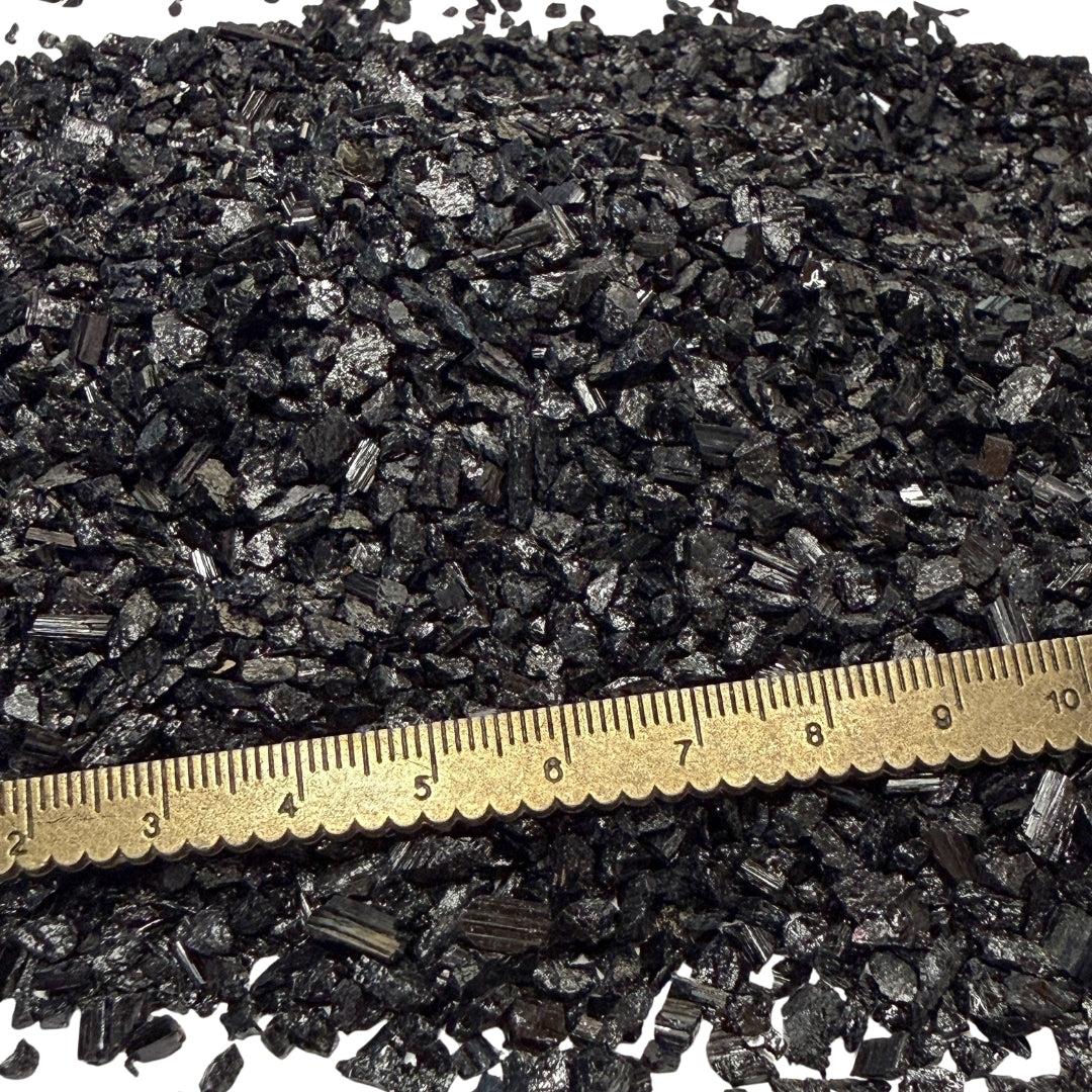Close-up of crushed black tourmaline chips with a metric ruler for scale on a white background