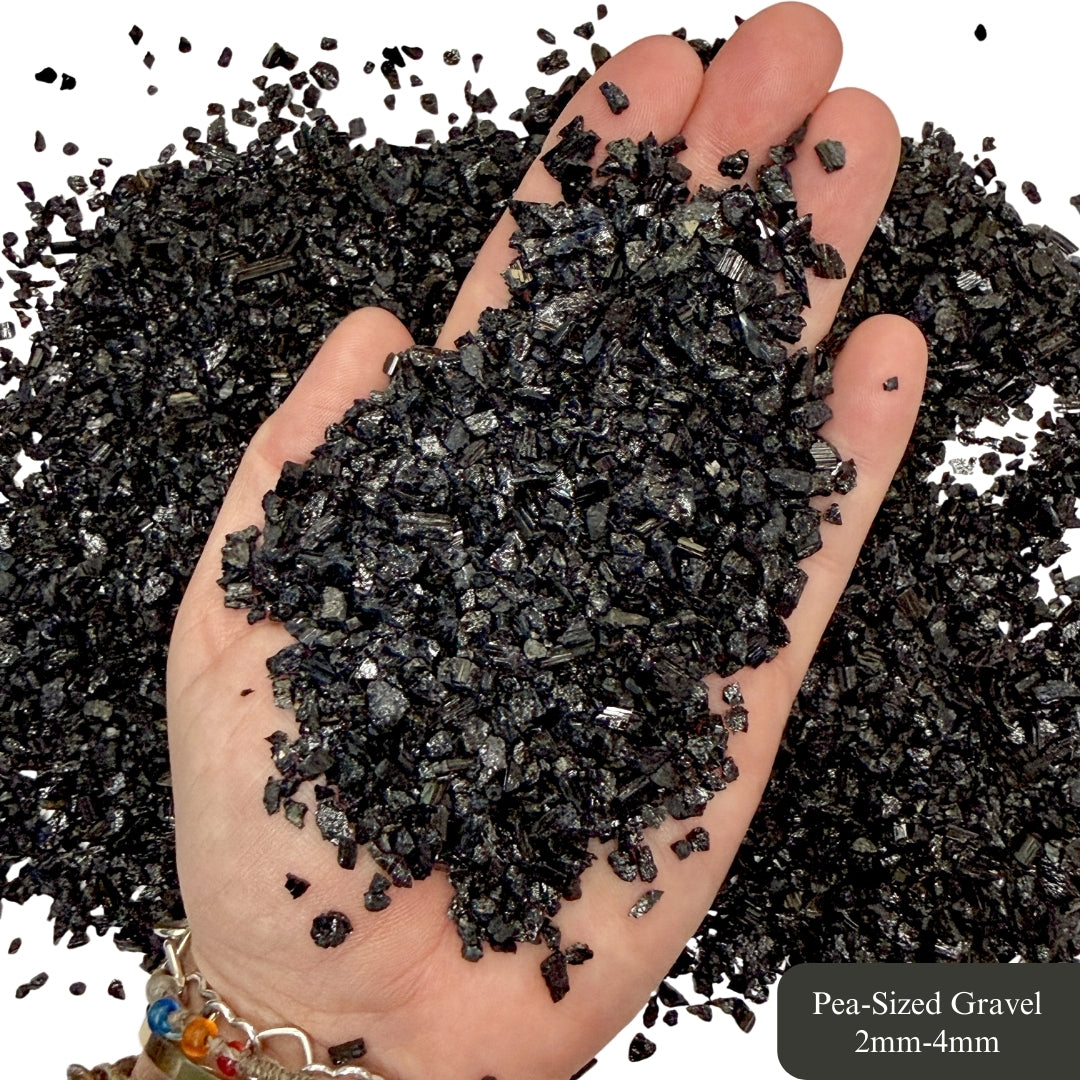 Hand holding rough, pea-sized black tourmaline with a white background