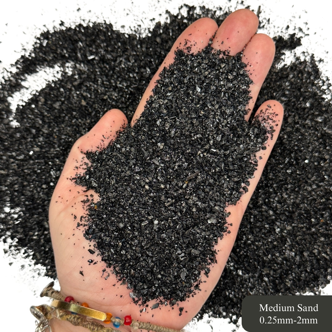 Hand holding black tourmaline sand with text indicating particle size 0.25mm-2mm.